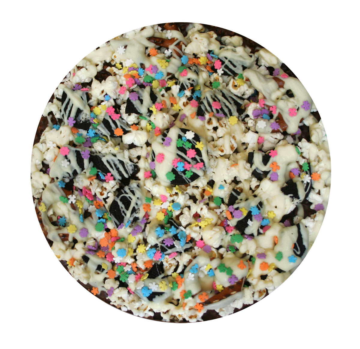 A circular close-up of a dessert or snack topped with white chocolate drizzle, dark chocolate pieces, and colorful star-shaped sprinkles on a white background.