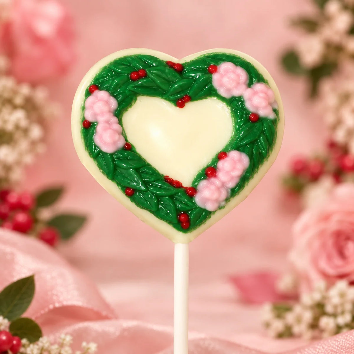 Wreath Heart Pollylop® — Chocolate Lollipop adorned with pink blossoms and green leaves on a white chocolate heart.
